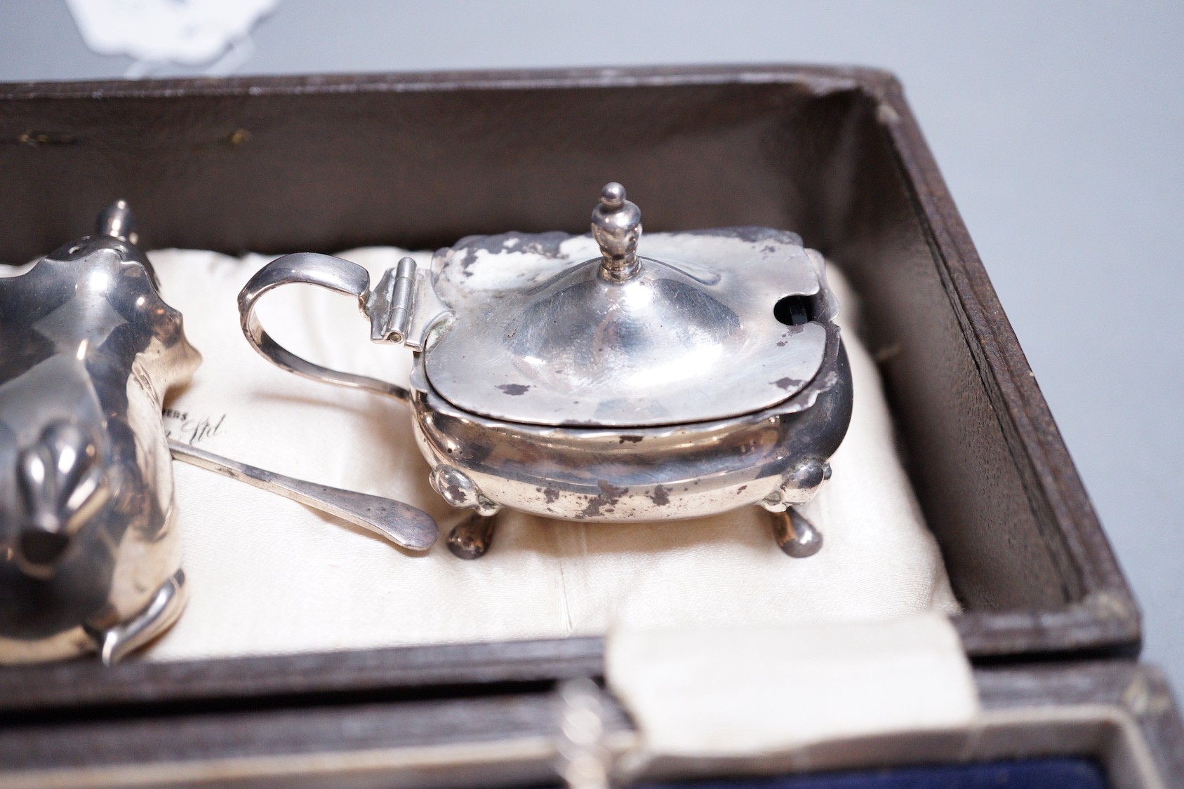 A cased George V silver three piece condiment set, two other silver condiments and a plated condiment.